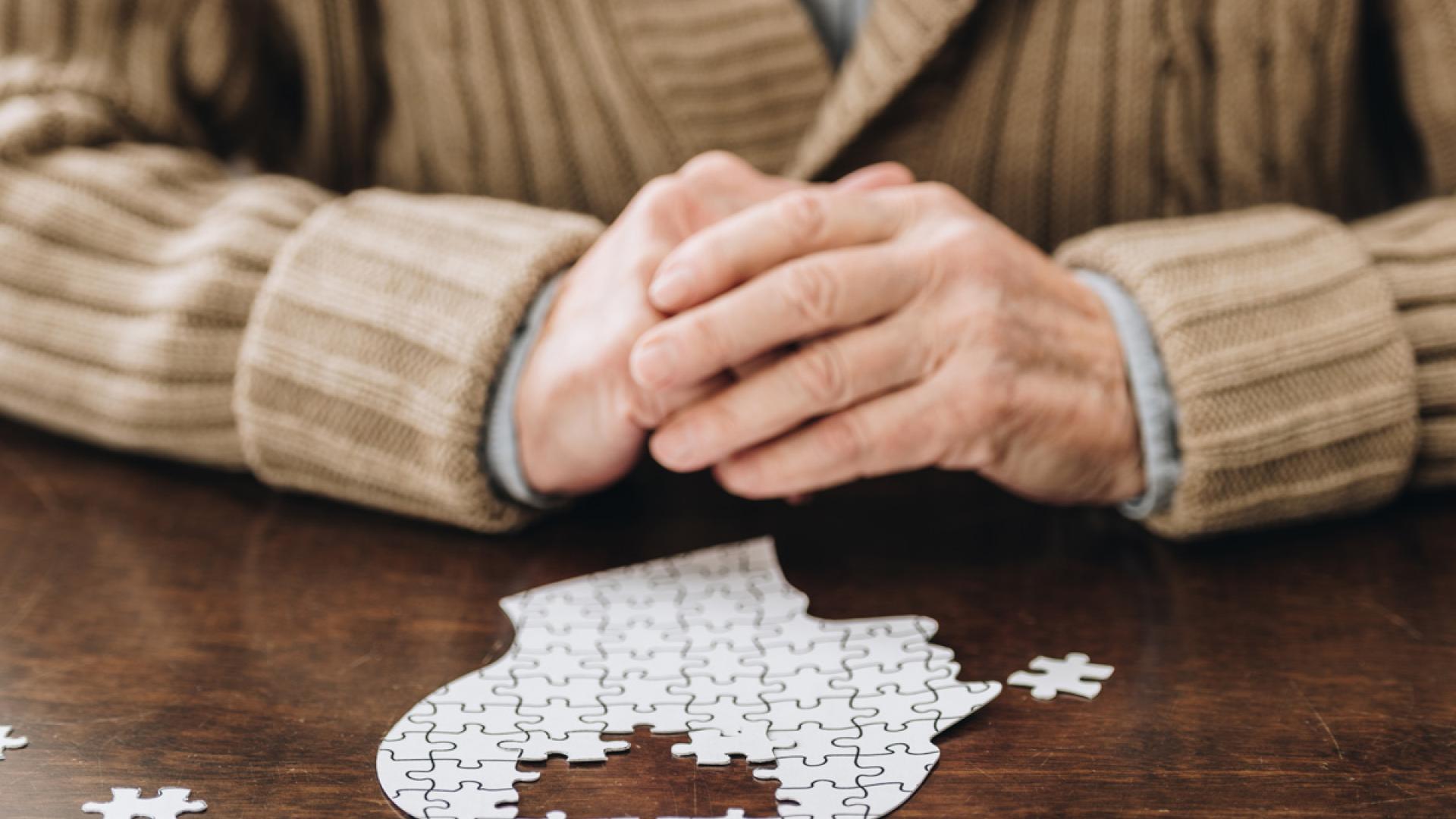 Senior person's hands doing a puzzle of a person's head