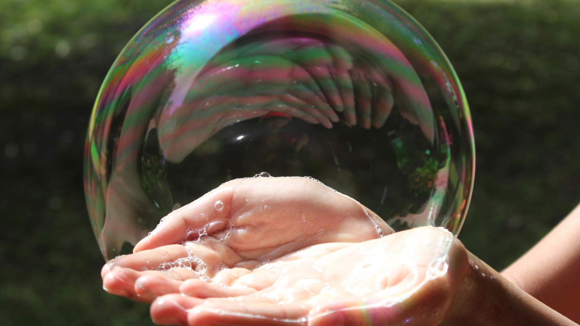 Hands holding giant bubble outside in park