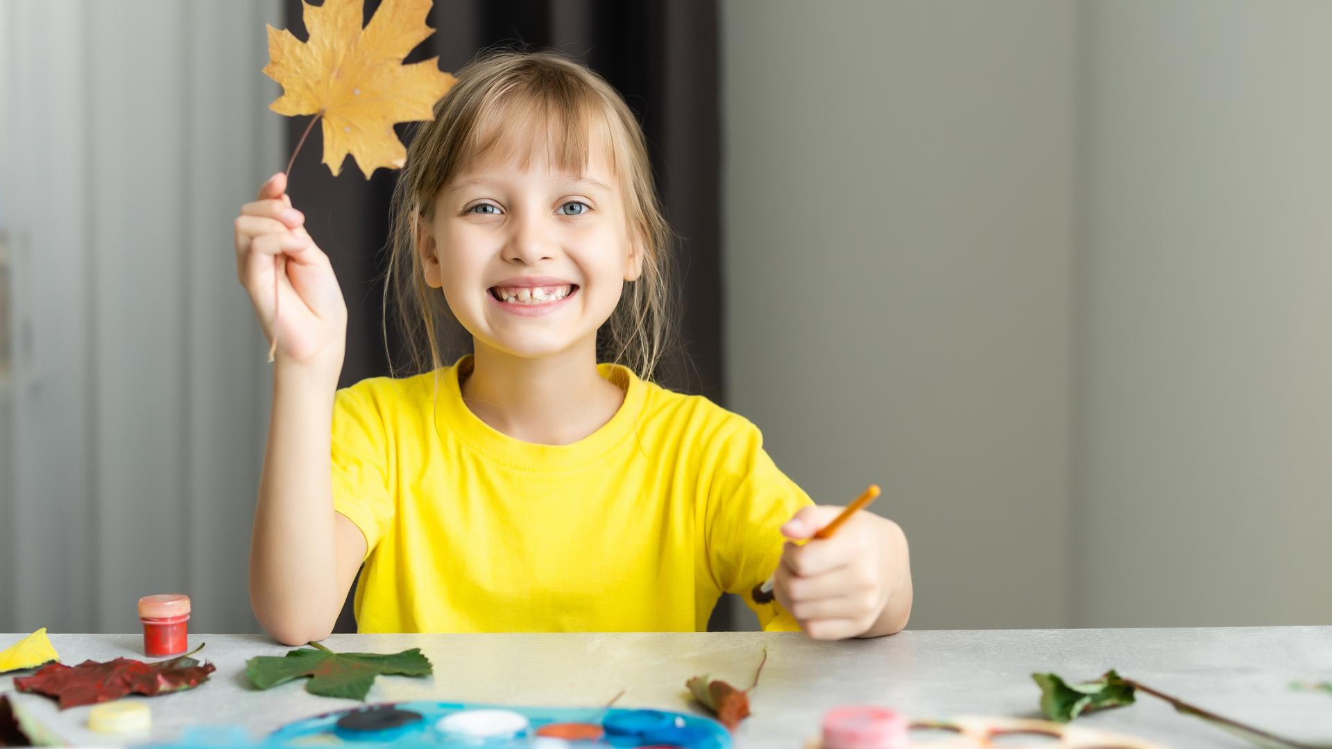Little girl smiling holding a maple leaf and a paint brush