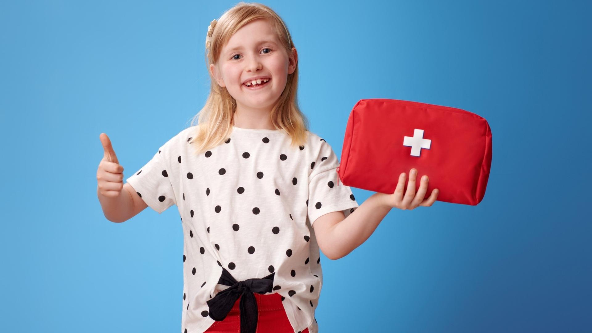 Girl with red pants and white shirt holding a first aid bag and giving the thumbs up