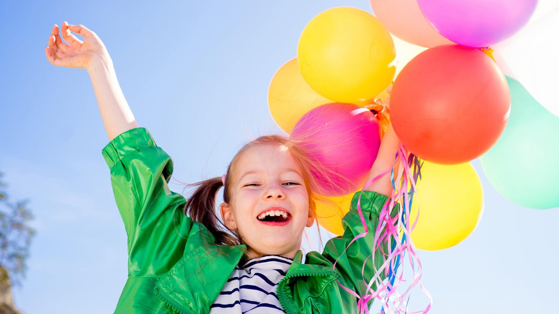 Little girl smiling holding a bunch of colourful balloons in the air