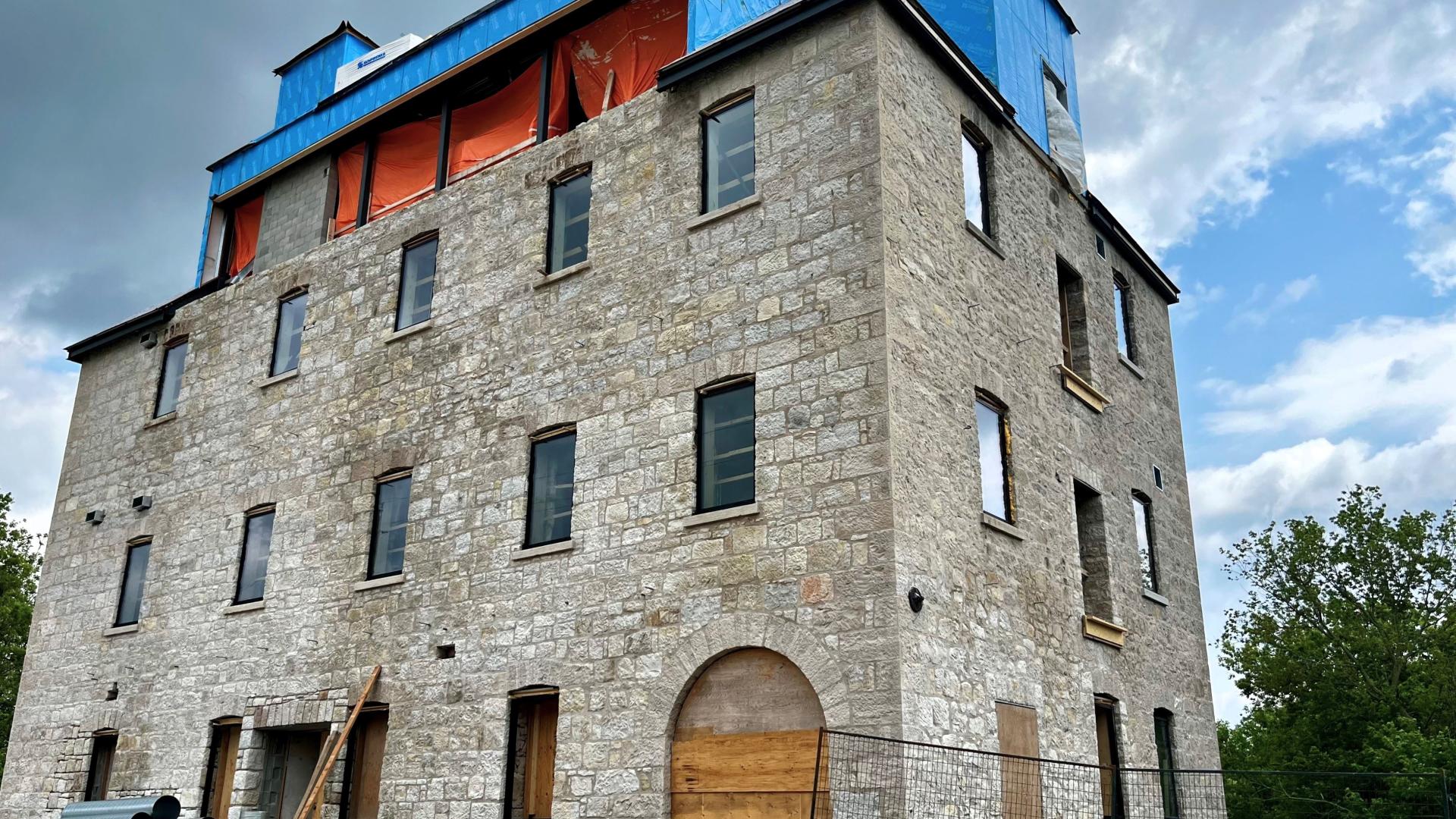 Exterior of historic Grist Mill with some new windows installed and top floor with blue insulation