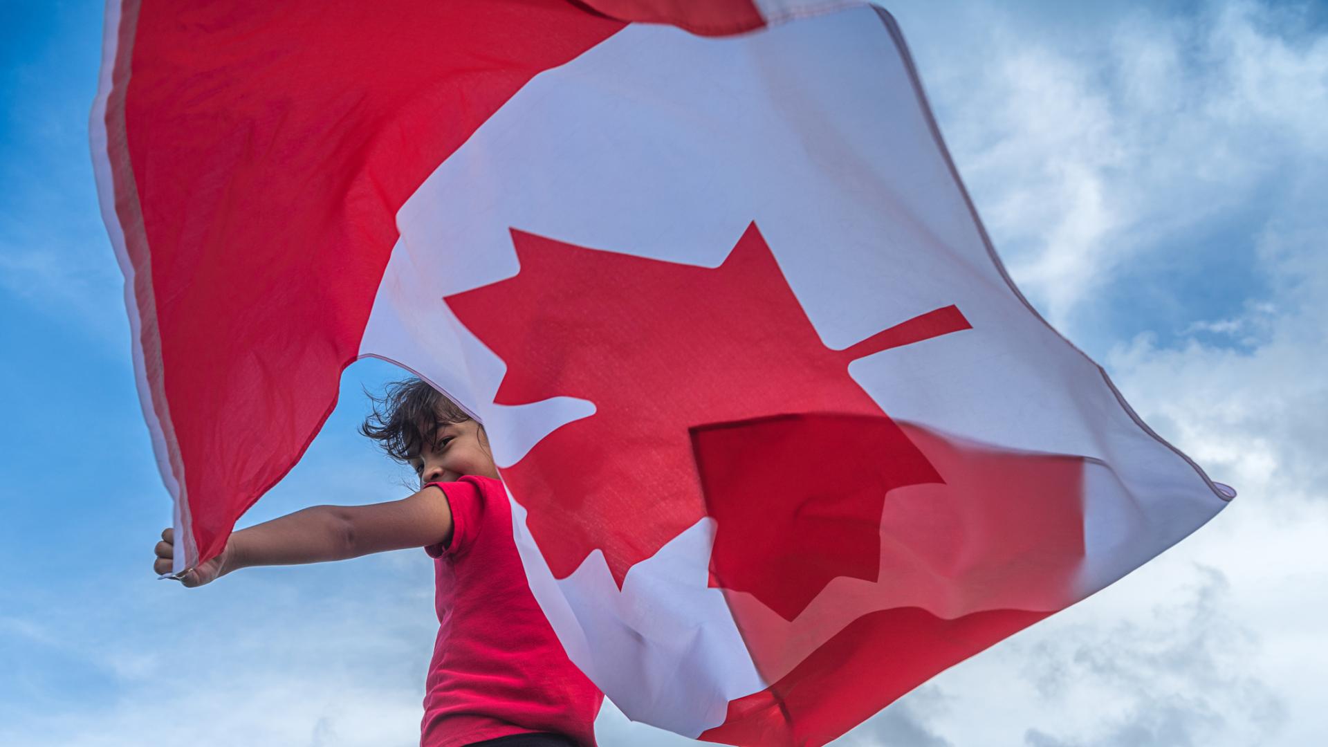 Girl holding a large Canada flag out behind her in the wind