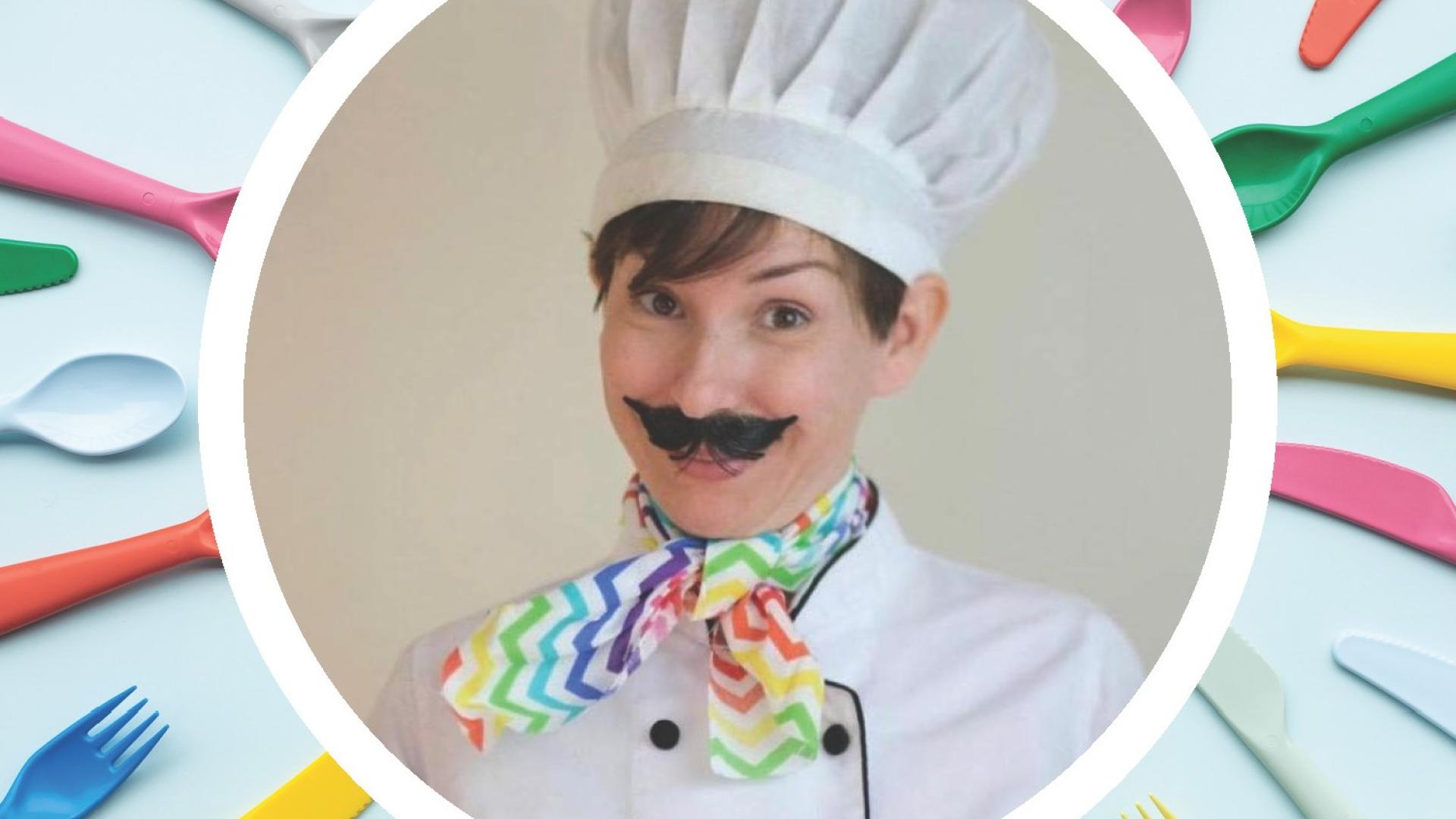 Woman dressed in a chef hat and fake moustache surrounded by colourful cutlery 