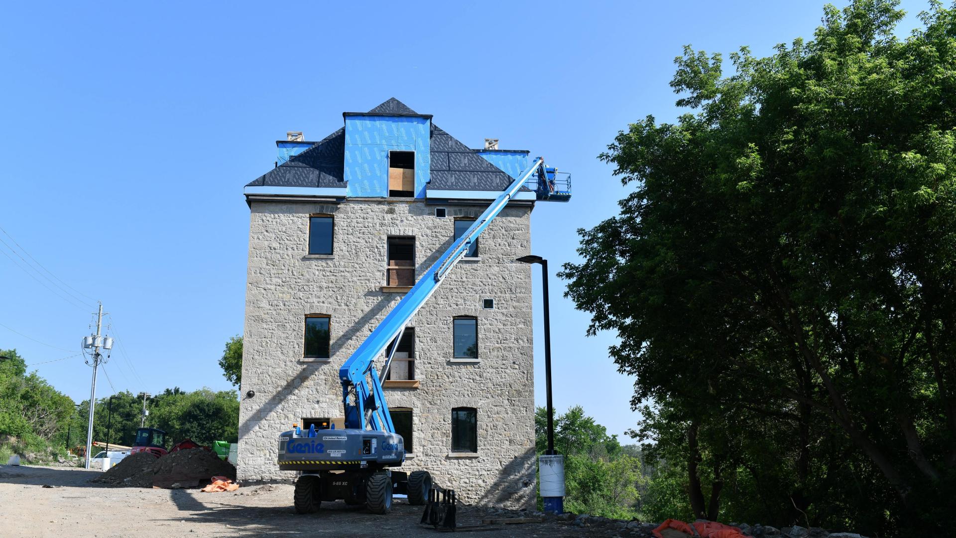 Three story stone building from the side with a blue crane reaching up to the new roof installation