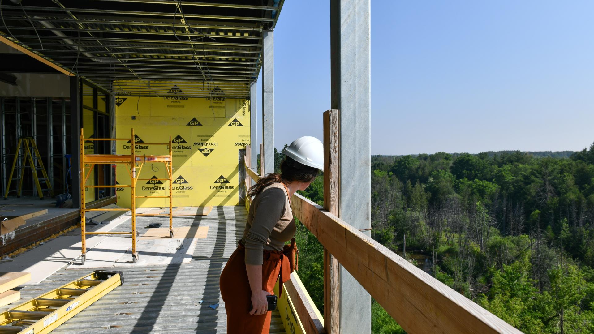 Person with a hard hat standing a looking out over forest from an upper balcony