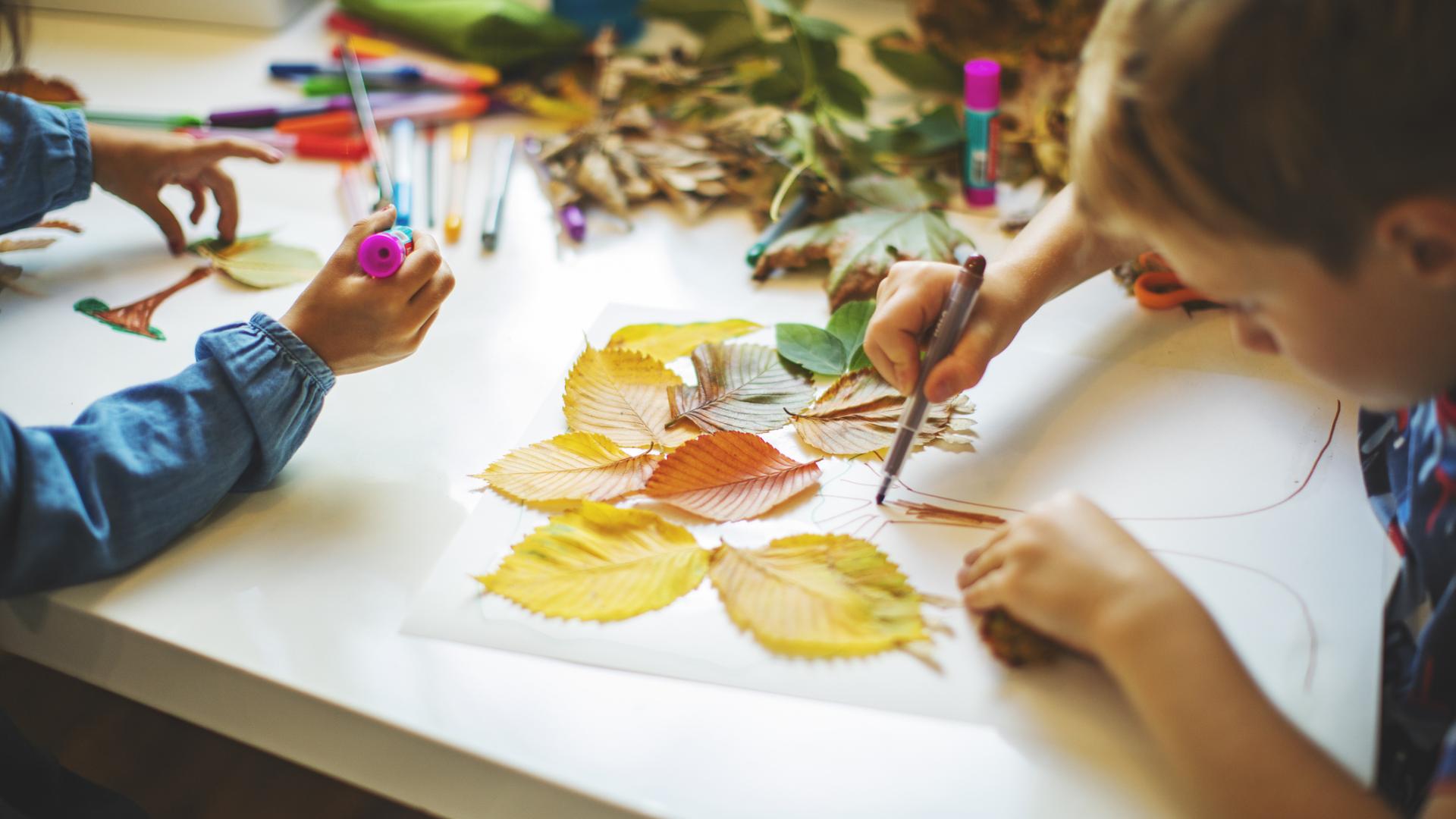 Little boy crafting a picture with fall leaves and glue