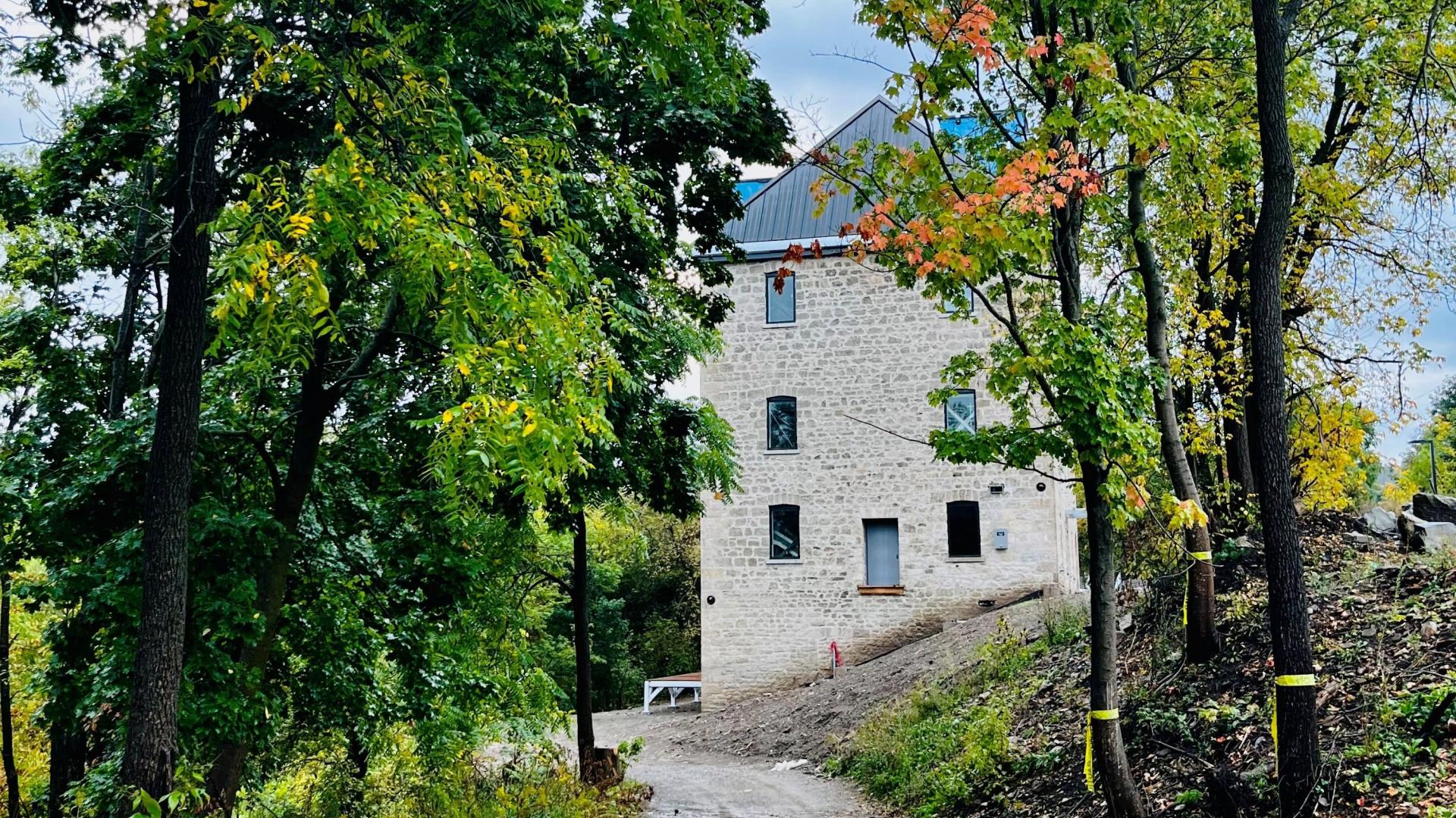 View of a four-story stone building down a dirt lane with fall trees on either side