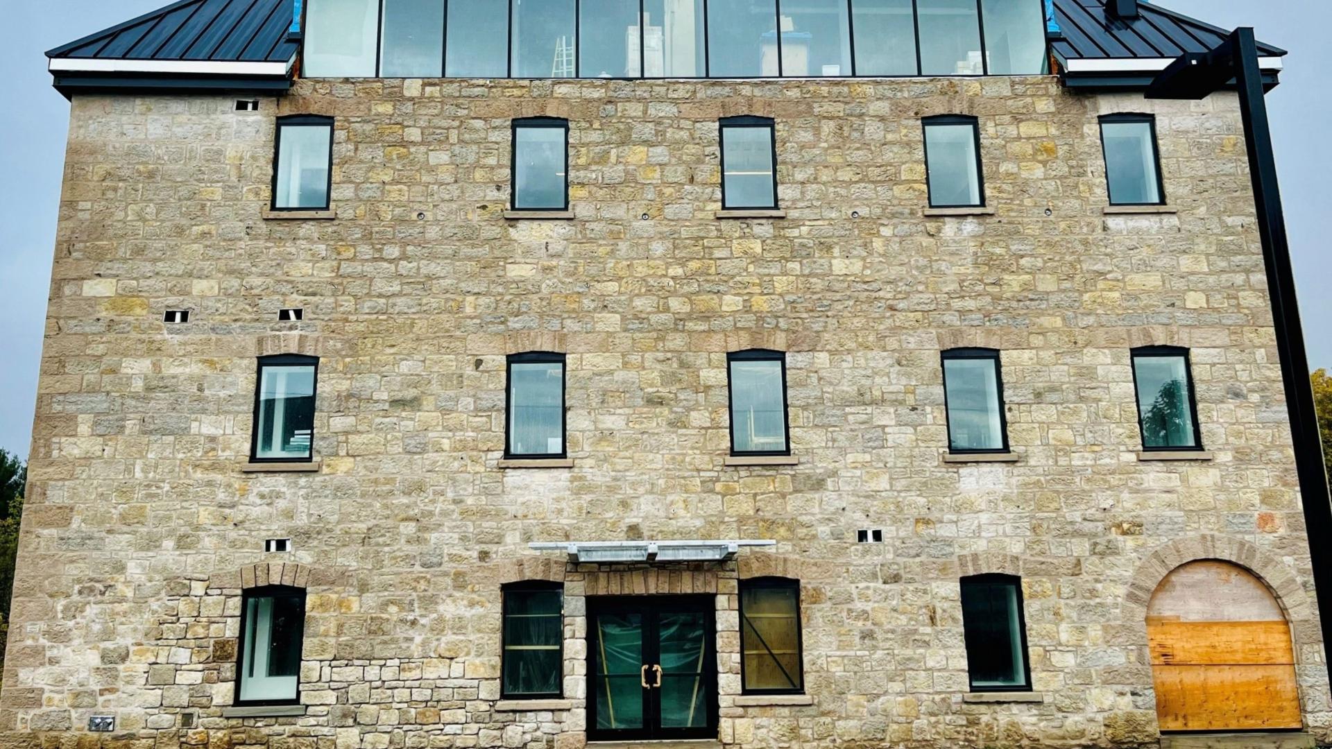 Front view of a three story stone building plus glassed in fourth floor under construction