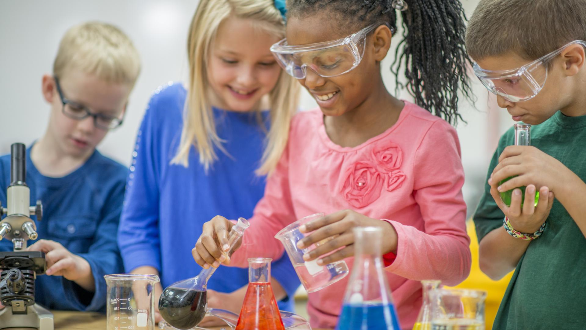 A group of kids in googles pouring coloured water into beakers