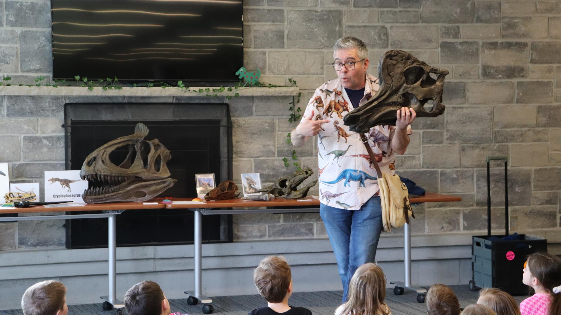 A person stands in front of a crowd of children showing them a dinosaur skull