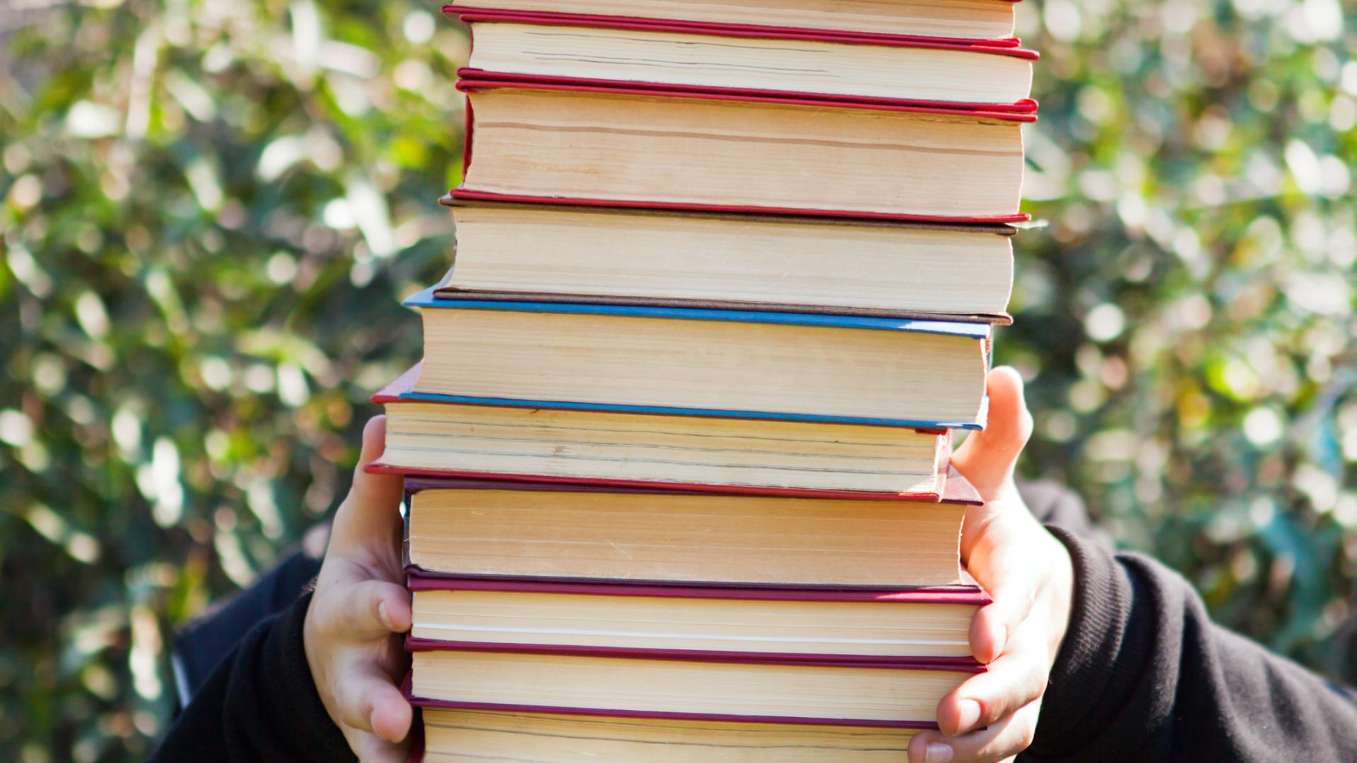 Person holding a large stack of books in front of their face