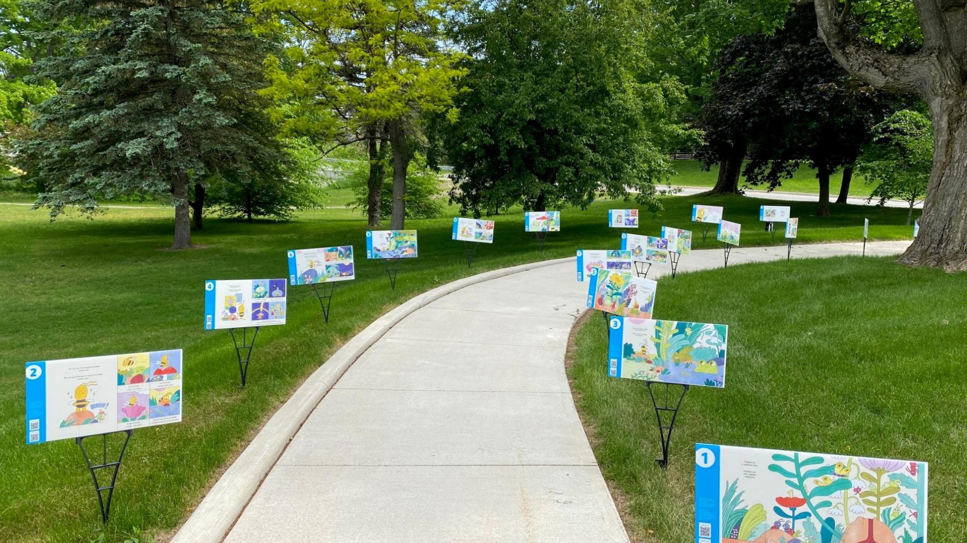 Photo of pages from a picture box are displayed as posters along a sidewalk and lawn