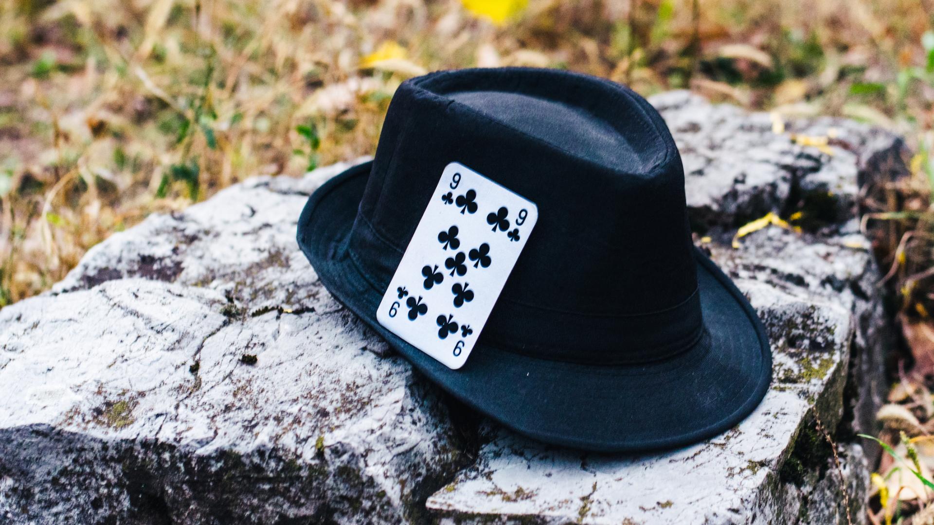 A photo of a black cowboy hat sitting on a rock with a playing card in its brim