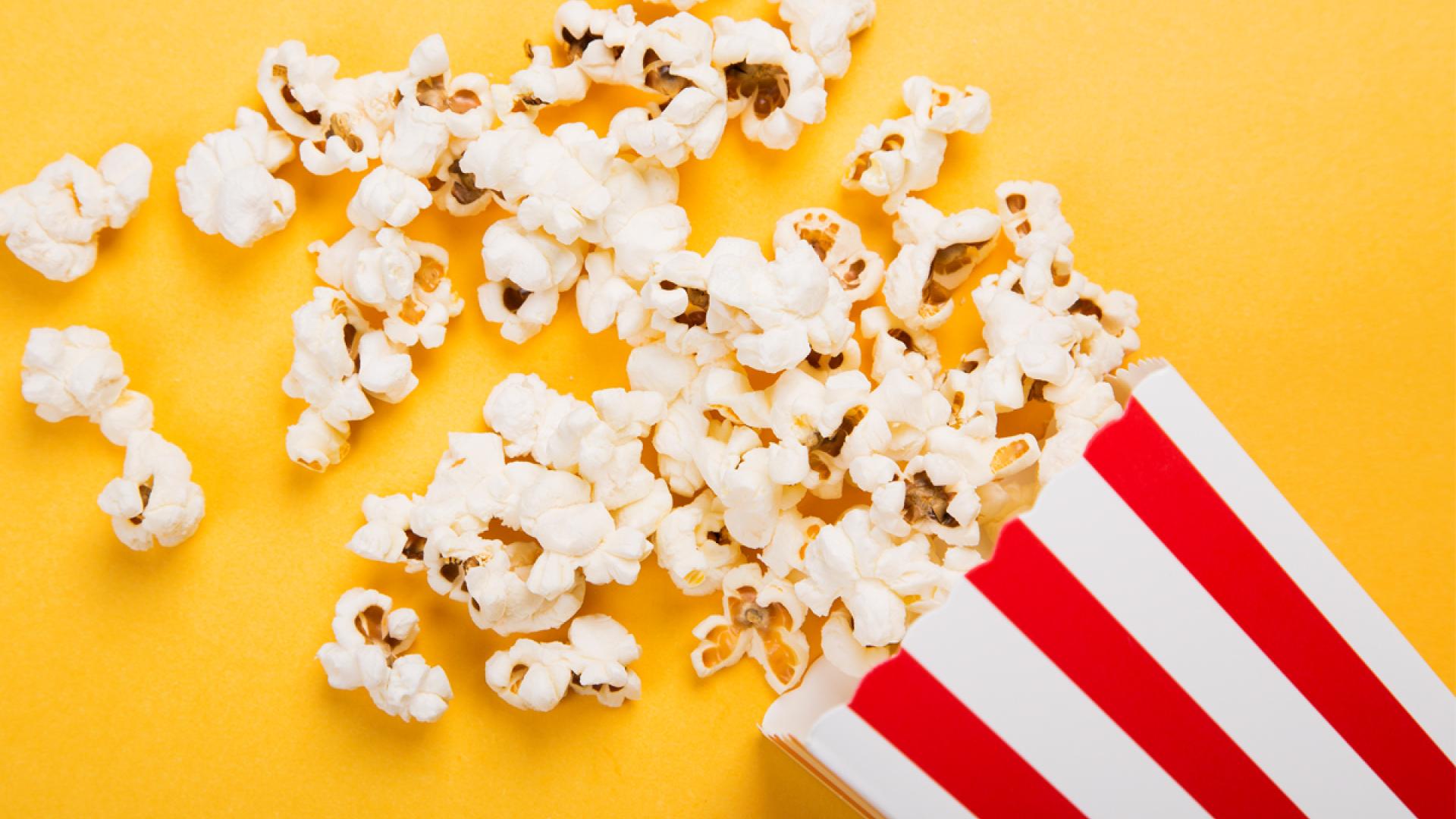 Red and white stripped bag of popcorn spilling out onto a yellow background