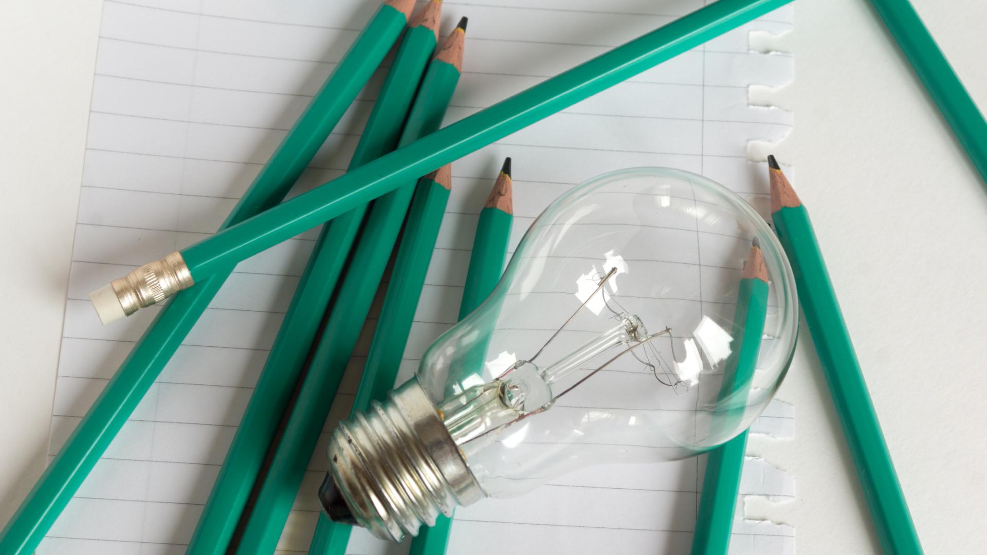 A lightbulb sits on paper surrounded by pencils