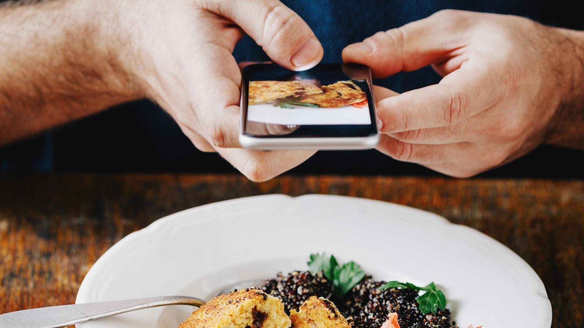 A photo of a man's hand holding a smart phone over a plate of food to take a photo