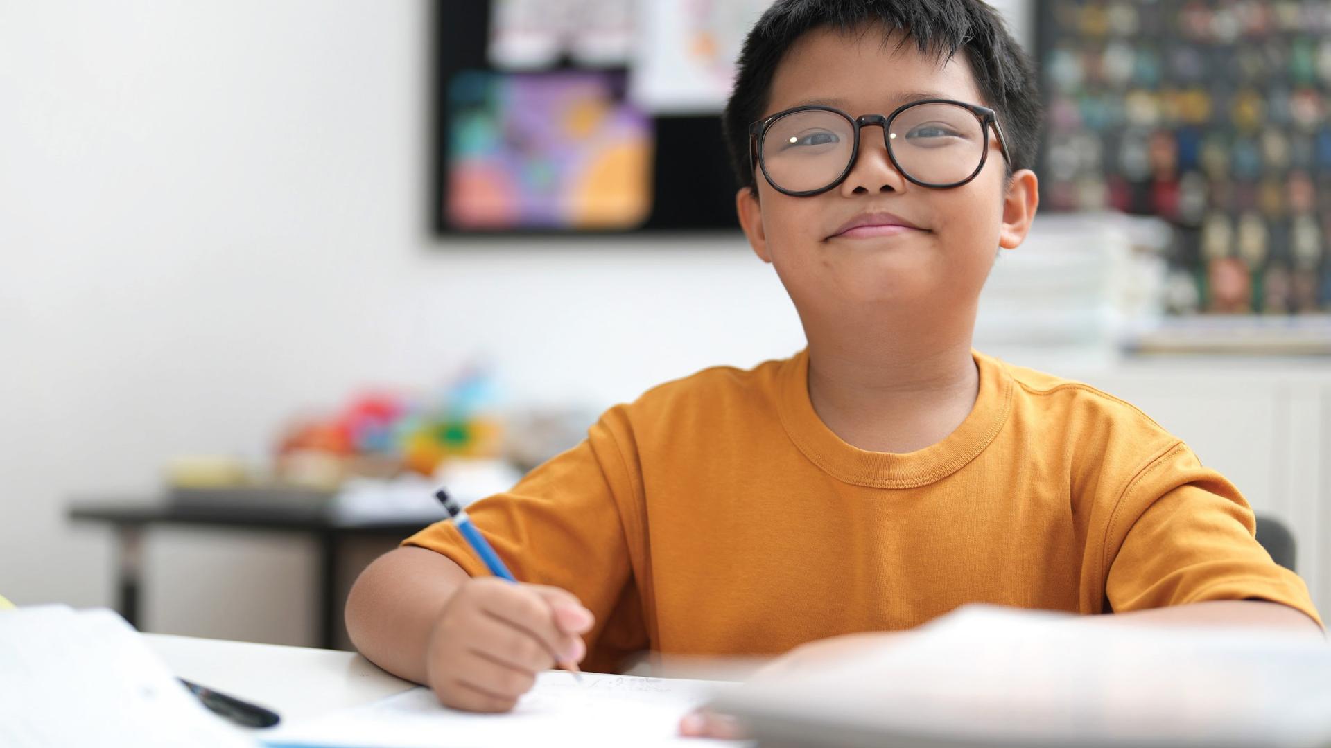 A photo of a smiling boy writing on paper with a pencil