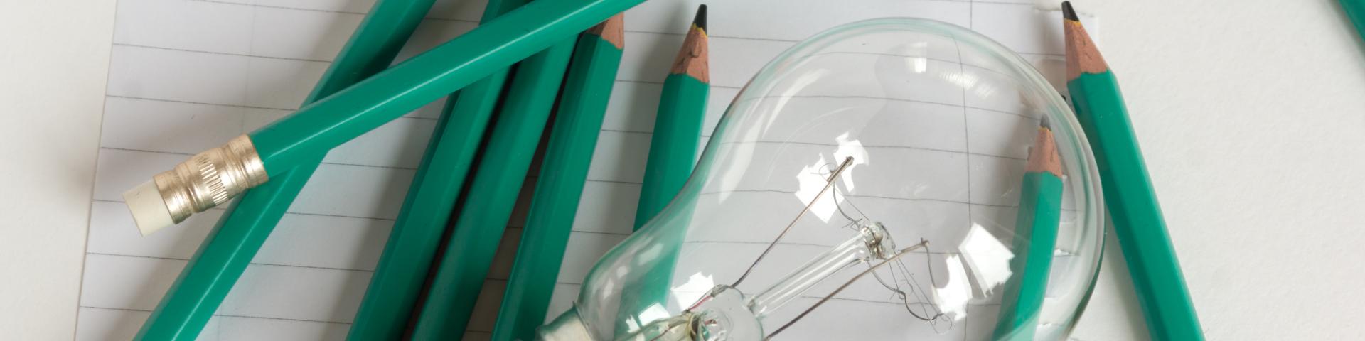 A lightbulb sits on paper surrounded by pencils