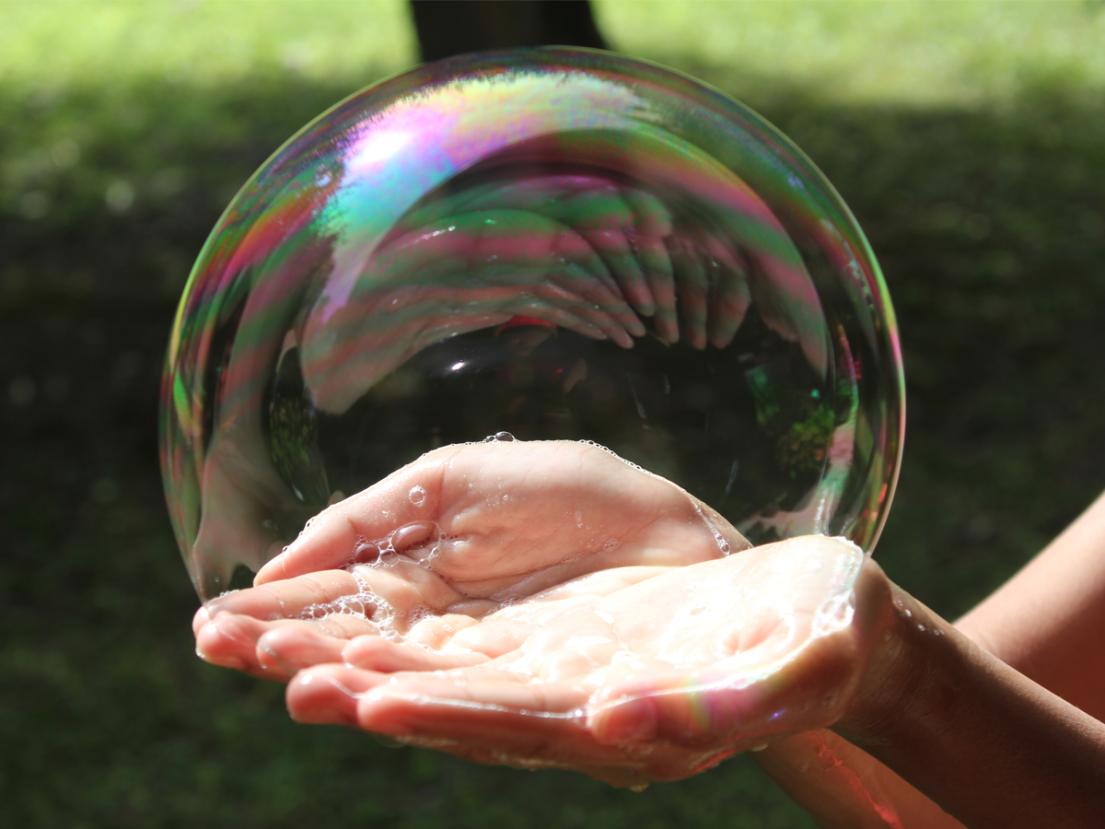 Hands holding giant bubble outside in park