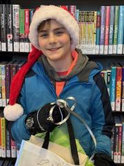 A young boy in a Santa hat smiles in front of a bookcase