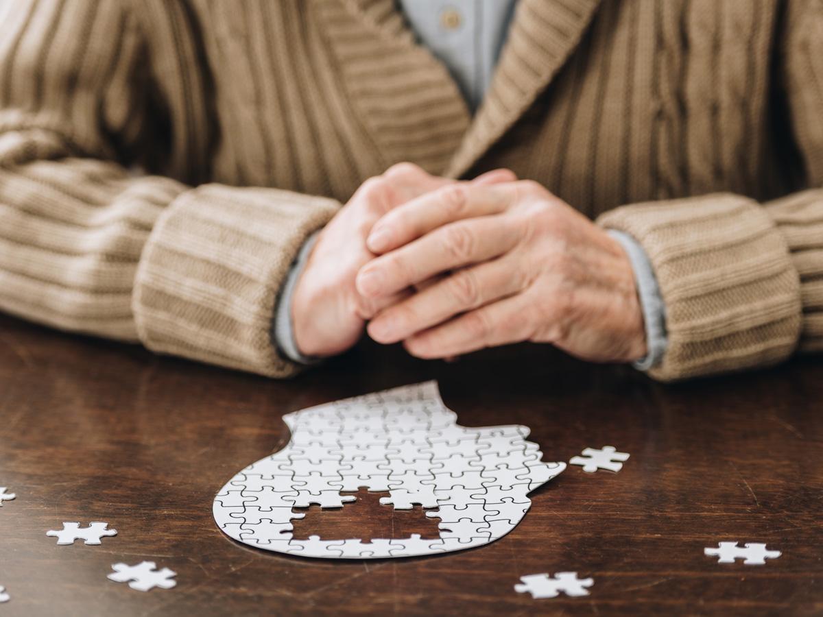 Senior person's hands doing a puzzle of a person's head