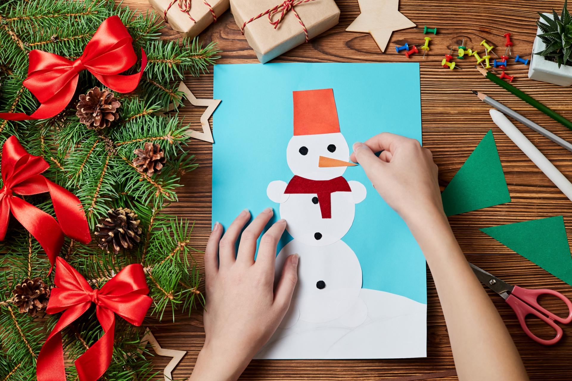 Hands making a snowman craft on a table with Christmas garland and red bows