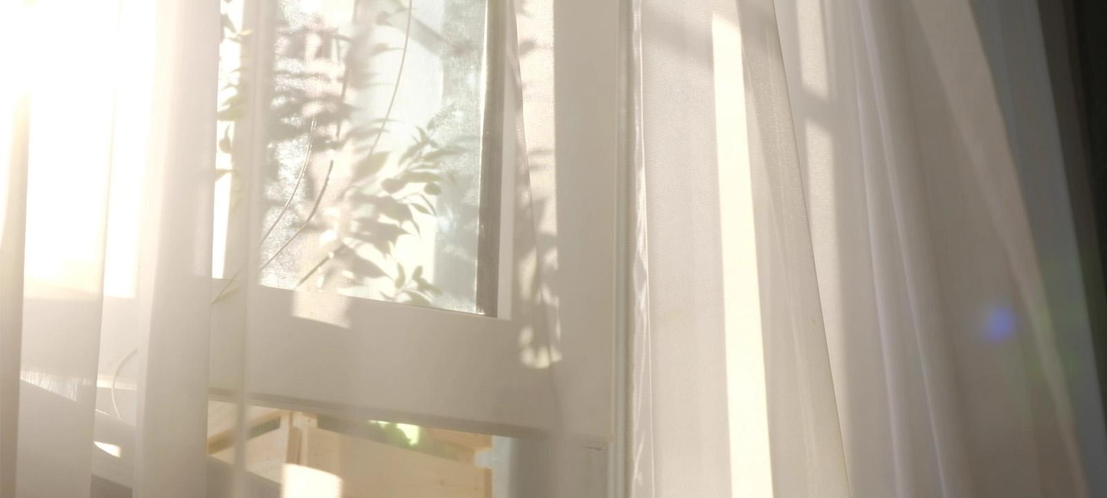 Window with white curtains and sunshine pouring in