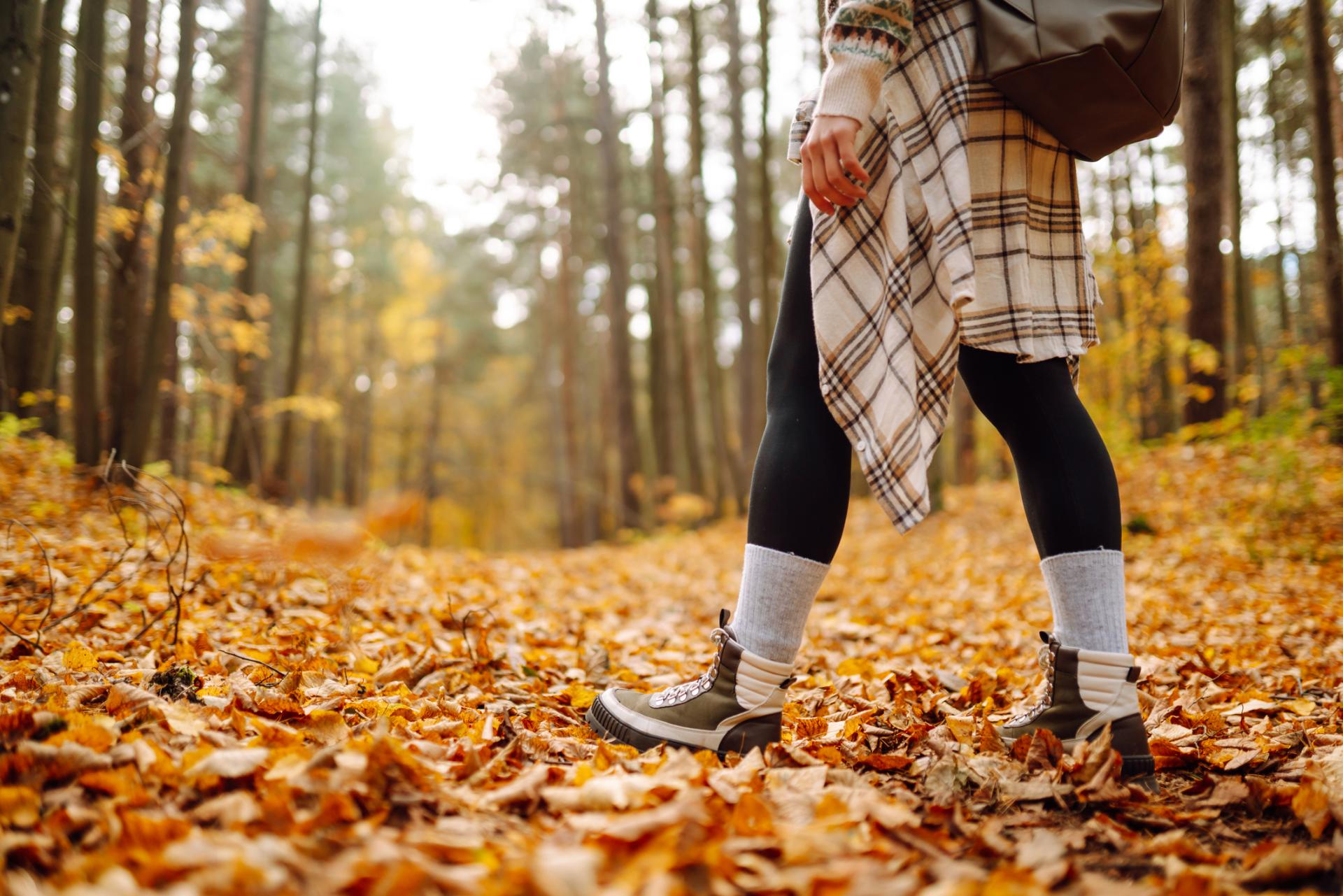 A hiker stands with fall leaves on the ground and autumn trees to either side of a walking trail